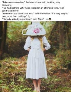 a woman in a white dress and hat standing in the woods with an umbrella over her head