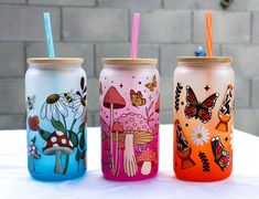 three colorful glass cups with straws and lids are sitting on a white tablecloth