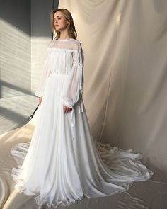 a woman standing in front of a white backdrop wearing a long dress with sheer sleeves