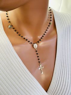 This is a stunning 14 karat gold filled charmed rosary inspired necklace. This necklace consist of 3.5 mm faceted onyx beads on 14k gold filled chain , four religious gold filled charms with a miraculous center and crucifix cross. This beautiful crucifix cross measures 28X 16 MM. Miraculous medal measures 16 X 13 MM and is double sided. The charms attached all are 14 karat gold filled. Tiny Saint Benedict medallion measures 10MM, our Lady of Guadalupe charm measures 9MM, pavé crystal Hamsa charm measures 11 MM and evil eye charm measures 11 X9MM. There is a spring clasp in back with a 2 inch adjustable length. Necklace on model is a 16-18 inch length. This is completely 14 karat gold filled.  Comes in a gift box ready to present. If you would like a different gemstone or crystal please sen Spiritual Necklace With Miraculous Medal And Round Beads, Crucifix Jewelry With Black Beads As Gift, Spiritual Black Necklaces With Charms, Black Beaded Crucifix Jewelry, Black Rosary Necklace, Rosary Inspired Necklace, Black Rosary, 14kt Gold Jewelry, Rosary Style Necklace