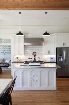 a kitchen with white cabinets and an island in front of a refrigerator freezer, stove top oven and dining room table