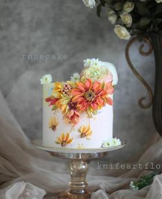 a white cake with orange and yellow flowers on it sitting on top of a table