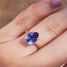 a woman's hand holding a ring with a large blue stone in the middle