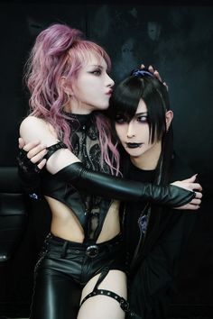 two women with pink hair and black leather clothes are hugging each other in front of a dark background