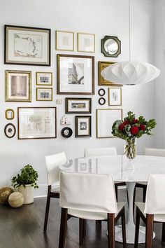 a white dining room table surrounded by framed pictures and vases with flowers on it