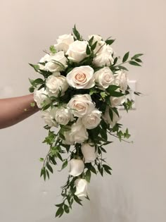 a bouquet of white roses and greenery is being held by someone's hand