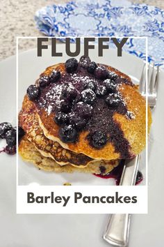 pancakes with blueberries and powdered sugar are on a plate next to a fork