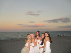 four women standing together on the beach at sunset