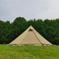 a tent pitched up in the middle of a field next to some bushes and trees