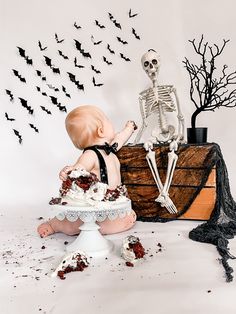 a baby sitting on top of a cake in front of a fake skeleton and bats