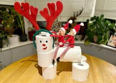 two elfs are sitting on top of toilet paper roll holders with reindeer antlers