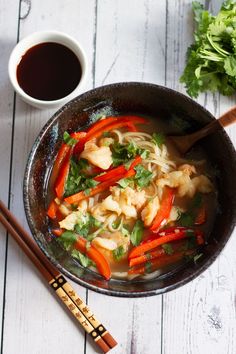 a bowl filled with noodles and vegetables next to chopsticks on top of a table