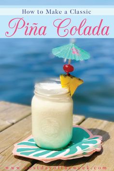 a pina colada drink sitting on top of a wooden table next to the ocean