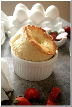 a pastry in a white dish with strawberries on the side and an egg shell behind it