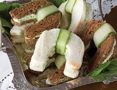 cucumber sandwiches are arranged on top of leafy greens in a silver tray