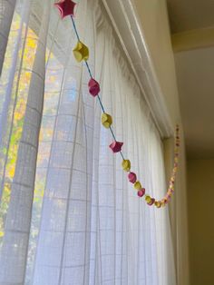 a string of paper stars hanging from a window sill in front of a curtain