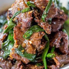 a white bowl filled with meat and greens on top of a tablecloth covered table