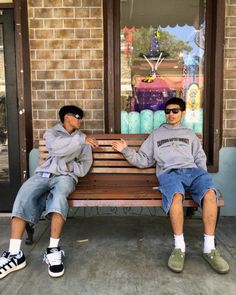 two young men sitting on a bench in front of a store with their hands together