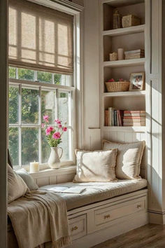 a window seat with pillows and flowers on it in front of a bookshelf