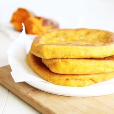 three pancakes sitting on top of a white plate next to a wooden cutting board with oranges in the background