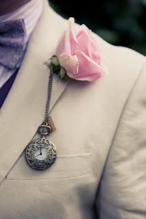 a man wearing a white suit with a pink rose attached to the lapel of his jacket