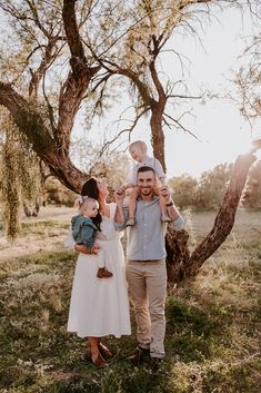 a man and woman holding their baby up in the air while standing under a tree