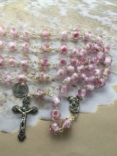 This pink womens rosary is very unique yet a very simple design. Each Our Father bead is decoratively wrapped with steel 22 gauge wire. The beads are made with Glass and Rondelle shaped which give a very unique design to the rosary. Each bead has a decorative rose flower embedded in the bead with a silver/gold decorative strip around it. The color is very light and elegant. This rosary would be the perfect gift a New Mother, Mother to be or any Mother as it has a centerpiece with Our Lady holdin Handmade Pink Spiritual Rosary, Mother's Day Rosary With 8mm Beads, Pink Rosary With Miraculous Medal As A Gift, Spiritual Gift Wire Wrapped Rosary, Spiritual Wire Wrapped Rosary As Gift, Mother To Be, Mother Mother, Catholic Rosary, Our Father