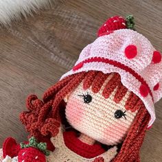 a crocheted doll wearing a red and white hat with strawberries on it