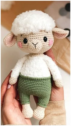 a hand holding a small stuffed sheep in green and white pants with pink nose eyes