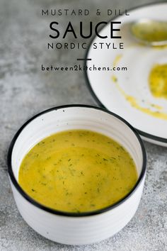 a white bowl filled with yellow sauce next to a plate full of green vegetables and broccoli