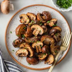 a white plate topped with mushrooms next to a fork and bowl of broccoli