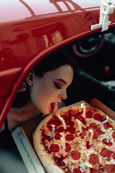 a woman blowing out candles on a pepperoni pizza in a box with the hood open