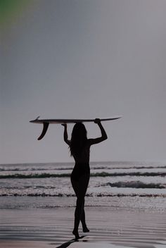 a woman holding a surfboard over her head while standing on the beach in front of the ocean