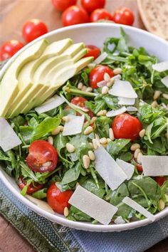 a salad with tomatoes, avocado and pine nuts in a white bowl on a wooden table