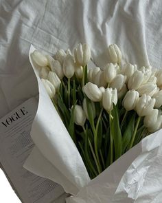 a bouquet of white tulips sitting on top of a bed next to an open book