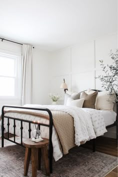 a bedroom with white walls and wood floors, a bed covered in blankets and pillows