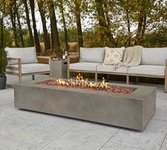 a fire pit sitting on top of a patio next to two couches and trees