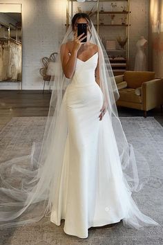 a woman in a wedding dress taking a selfie with her cell phone while wearing a veil