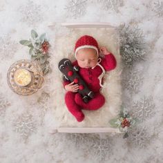 a newborn baby is sleeping next to a christmas ornament and holding a teddy bear