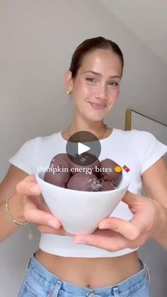 a woman holding a bowl filled with chocolate covered donuts