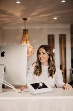 a woman sitting at a desk in front of a computer monitor with an ipad on it