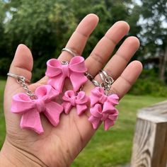 a hand holding three pink flower charms on it's fingers in front of some grass