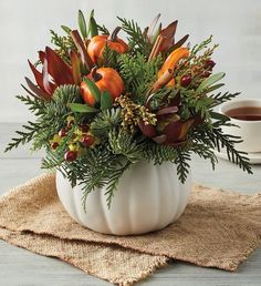 a white pumpkin filled with flowers and greenery next to a cup of hot chocolate