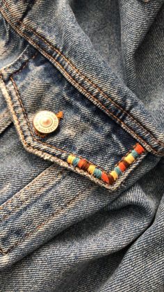 a button on the back of a pair of blue jeans with multicolored beads