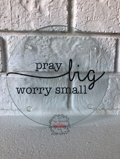 a glass sign that says pray big worry small on the side of a brick wall