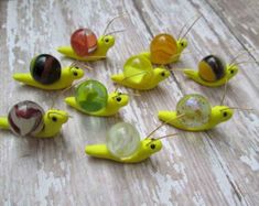 small yellow plastic snails sitting on top of a wooden table next to each other with different colored glass balls in them