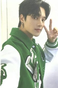 a young man in a green hoodie making the peace sign with his hand while standing next to a white wall