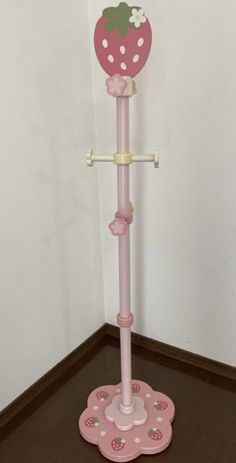 a pink umbrella stand with a strawberry on top and polka dots around the base, in front of a white wall