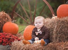 a toddler sitting on hay with pumpkins in the background