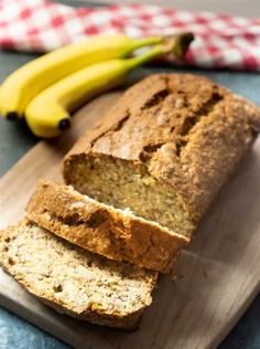 a loaf of banana bread sitting on top of a cutting board next to two bananas